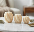 Three handmade twisted sphere soy wax candles in small, medium, and large sizes on a marble surface with eucalyptus leaves