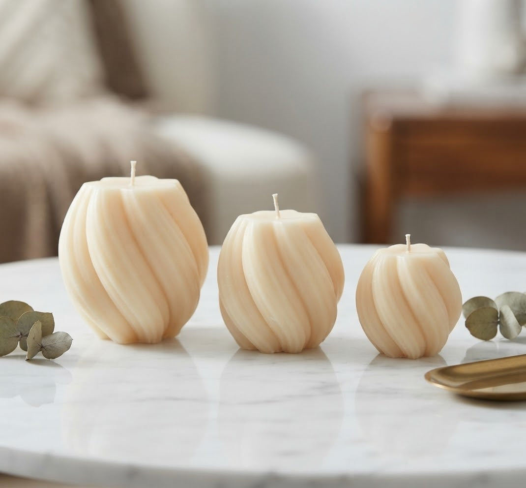 Three handmade twisted sphere soy wax candles in small, medium, and large sizes on a marble surface with eucalyptus leaves